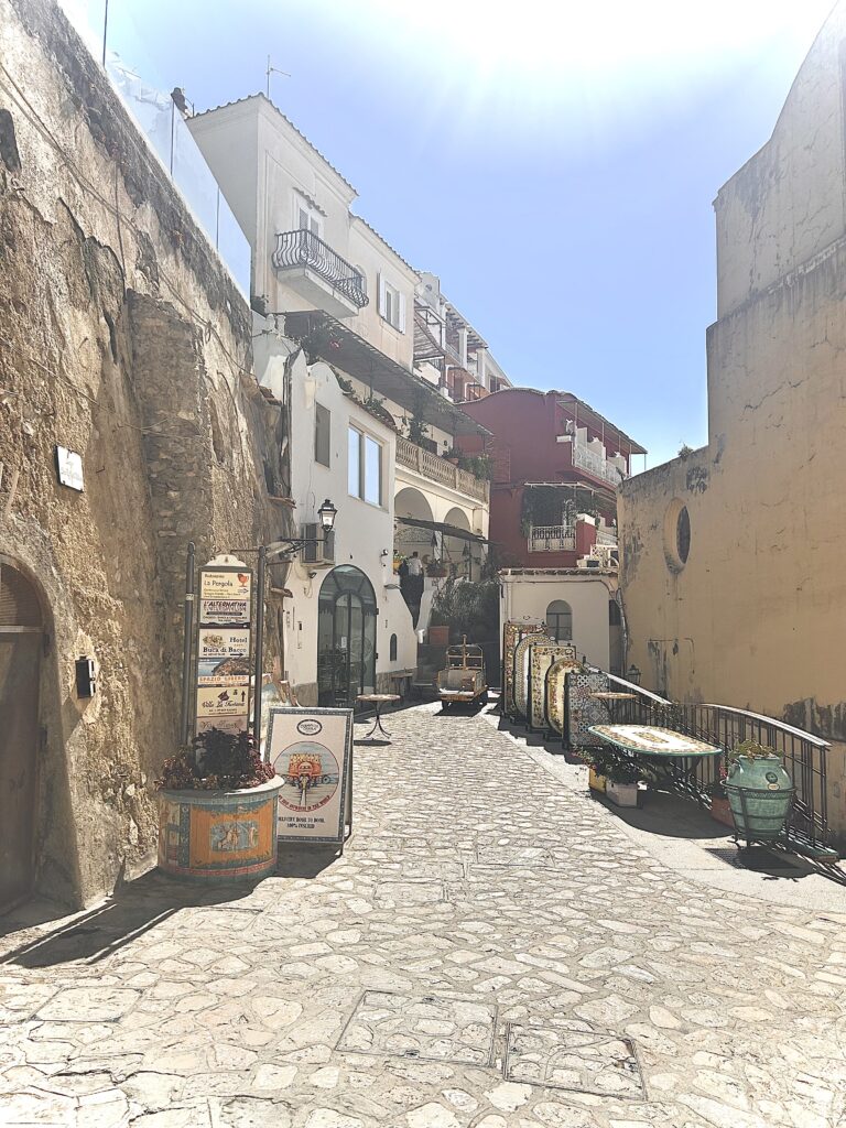 Sunlit stone walkway along the Amalfi Coast with coastal buildings and soft natural light