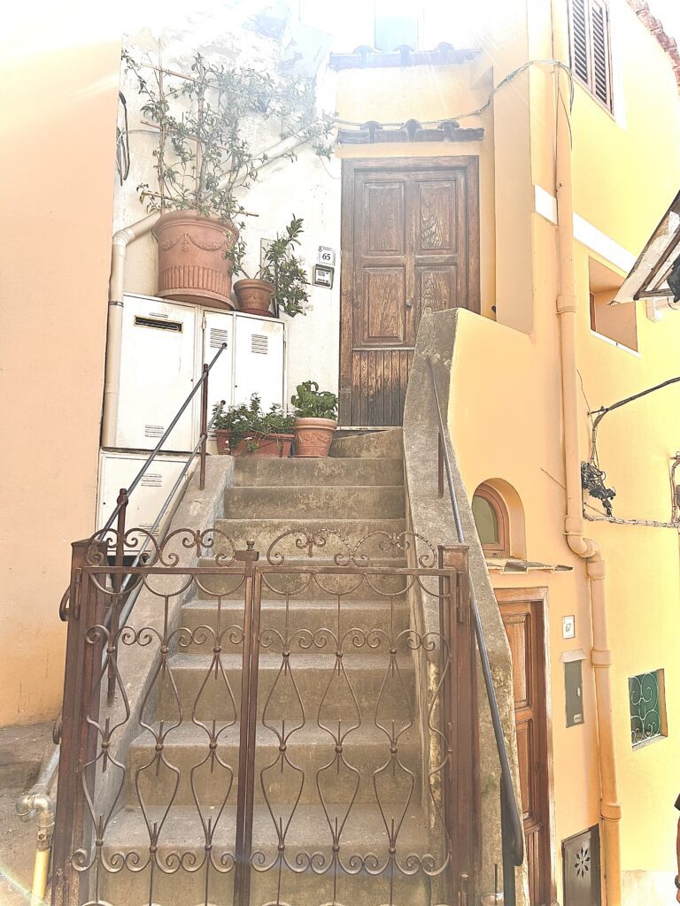 Sunlit stone walkway along the Amalfi Coast with coastal buildings and soft natural light
