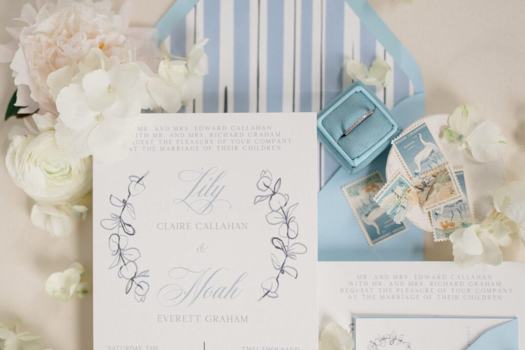 Coastal blue wedding invitation with floral illustration, vintage stamps, and soft line art flowers