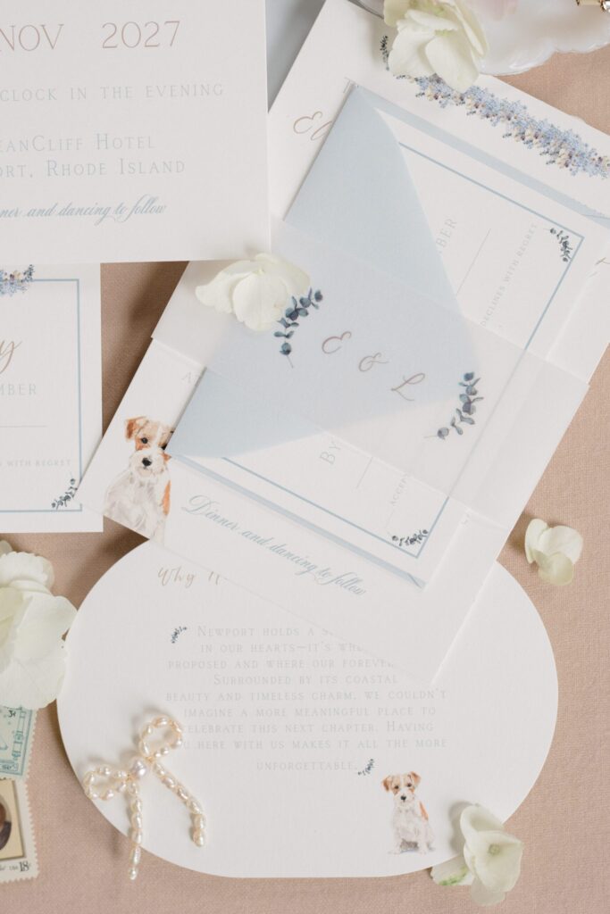 Wedding invitation suite with vellum wrap, soft blue envelope, and subtle dog illustration detail