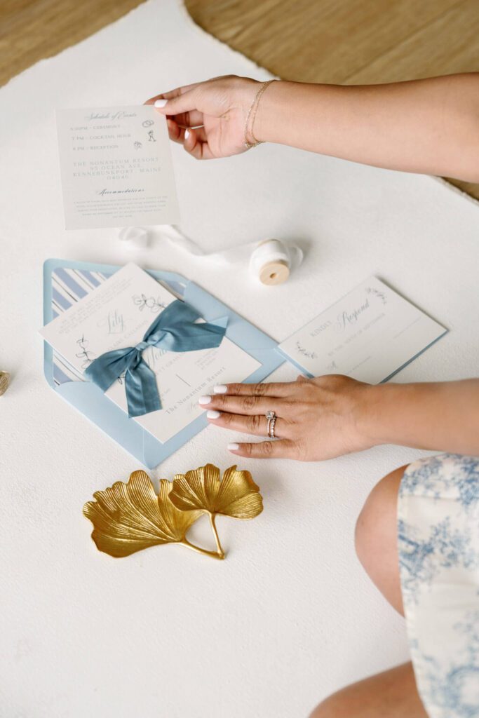 Styling a coastal blue wedding invitation flatlay with ribbon, envelope, and detail cards