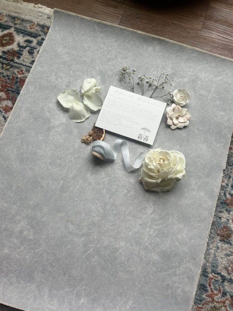 Minimal wedding invitation flatlay with florals, ribbon, and styling details on textured surface