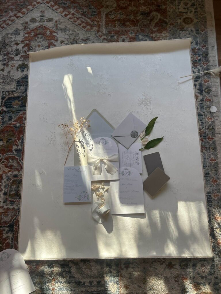 Wedding invitation flatlay setup with styling board, ribbon, florals, and paper goods
